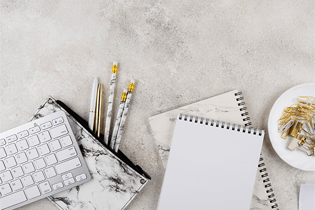 Bureau vu du dessus, avec des éléments de bureautique, dont un clavier, une trousse de laquelle sortent des stylos, des blocs, notes et une sous coupe contenant des trombones et des pinces