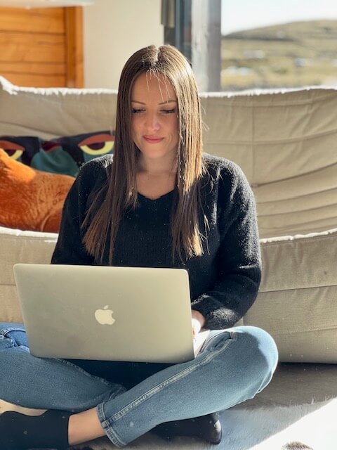 photo d'Estelle BELLANGER - rédactrice web - assise par terre, en tailleur, regardant l'écran d'un ordinateur portable sur ses genoux,