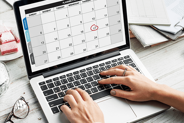 Mains d'une personne tapant sur le clavier d'un ordinateur portable dont l'écran affiche un calendrier