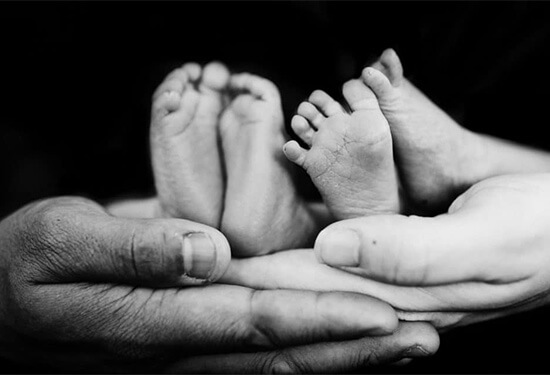 photo en noir et blanc de mains d'adultes soutenant des pieds de bébés